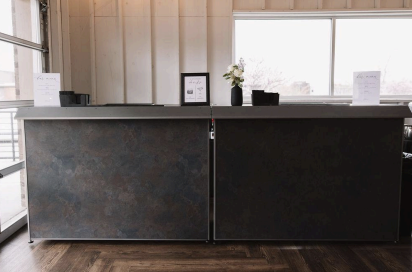 Sleek industrial-style bar at 14TENN event venue in Nashville, featuring a dark metal front, wood herringbone floors, modern signage, and natural light from large windows.